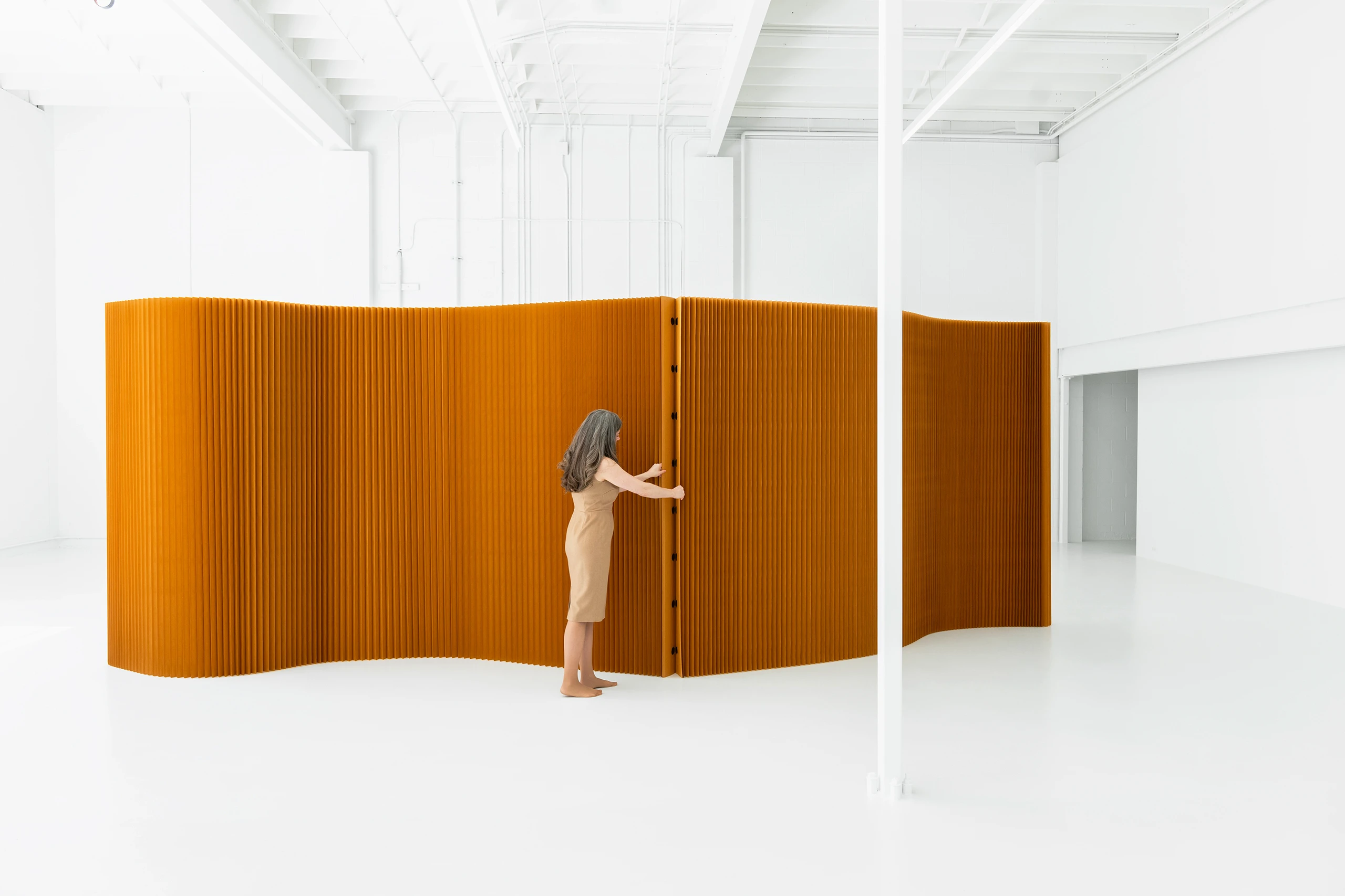 A woman connects two paper softwalls by their magnetic end panels.