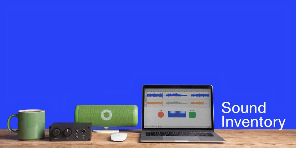 A modern music production workspace featuring a laptop with audio software, a speaker, and a mug.