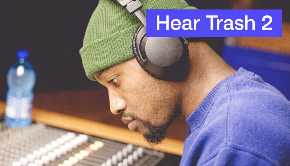 A music producer wearing a green beanie and headphones while working at a professional mixing console.