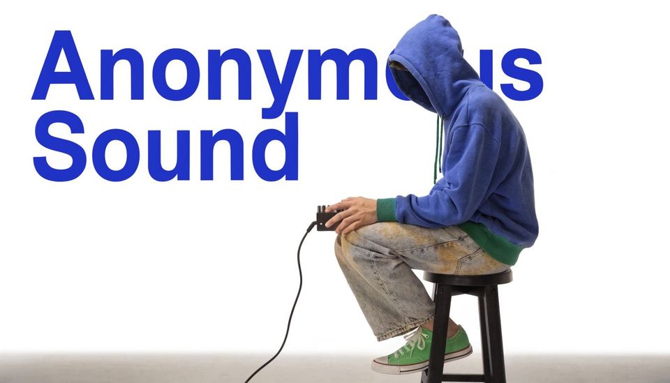A person in a blue hoodie and jeans sitting on a stool adjusting an audio effects pedal.