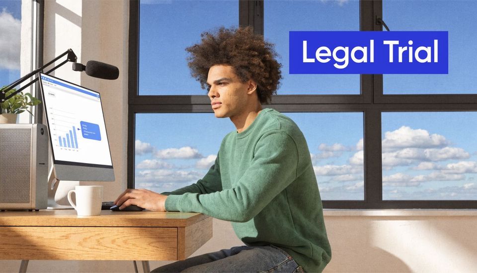 A young man with curly hair working on his computer in a bright home office setting.