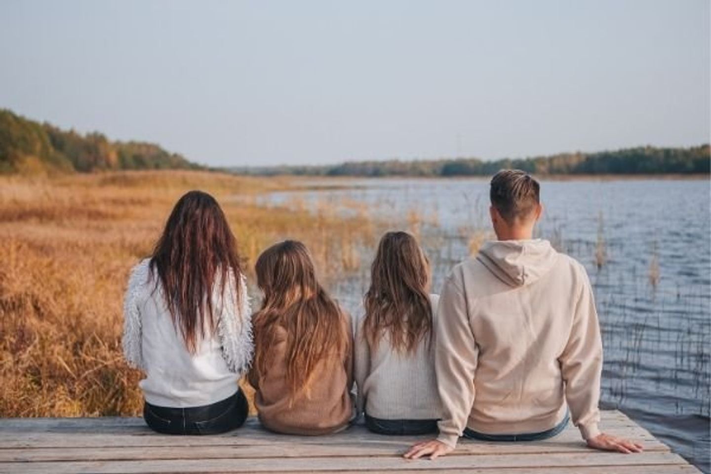 A family of four sitting together on a dock, looking out over the lake