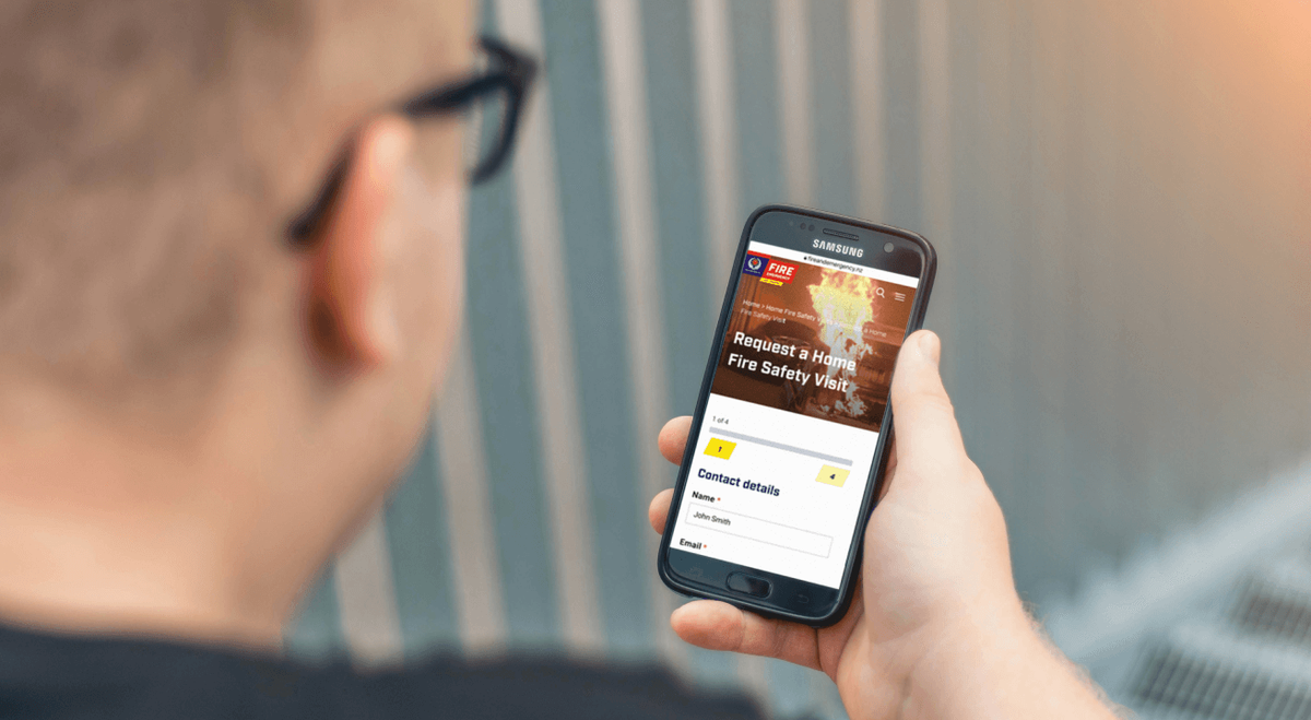 A picture taken overlooking a persons shoulder at their phone, which shows an image of the Fire Home Safety visit website