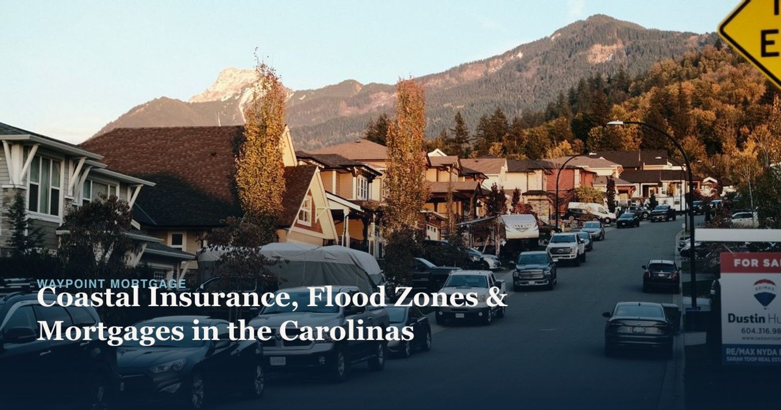 A serene suburban street lined with cars and mountain views under clear skies.