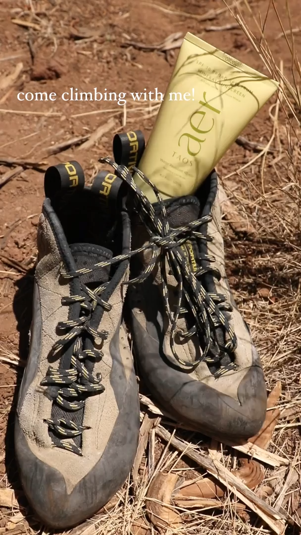 Well-worn climbing shoes on red dirt with a tube of Aer body wash