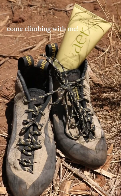 Well-worn climbing shoes on red dirt with a tube of Aer body wash