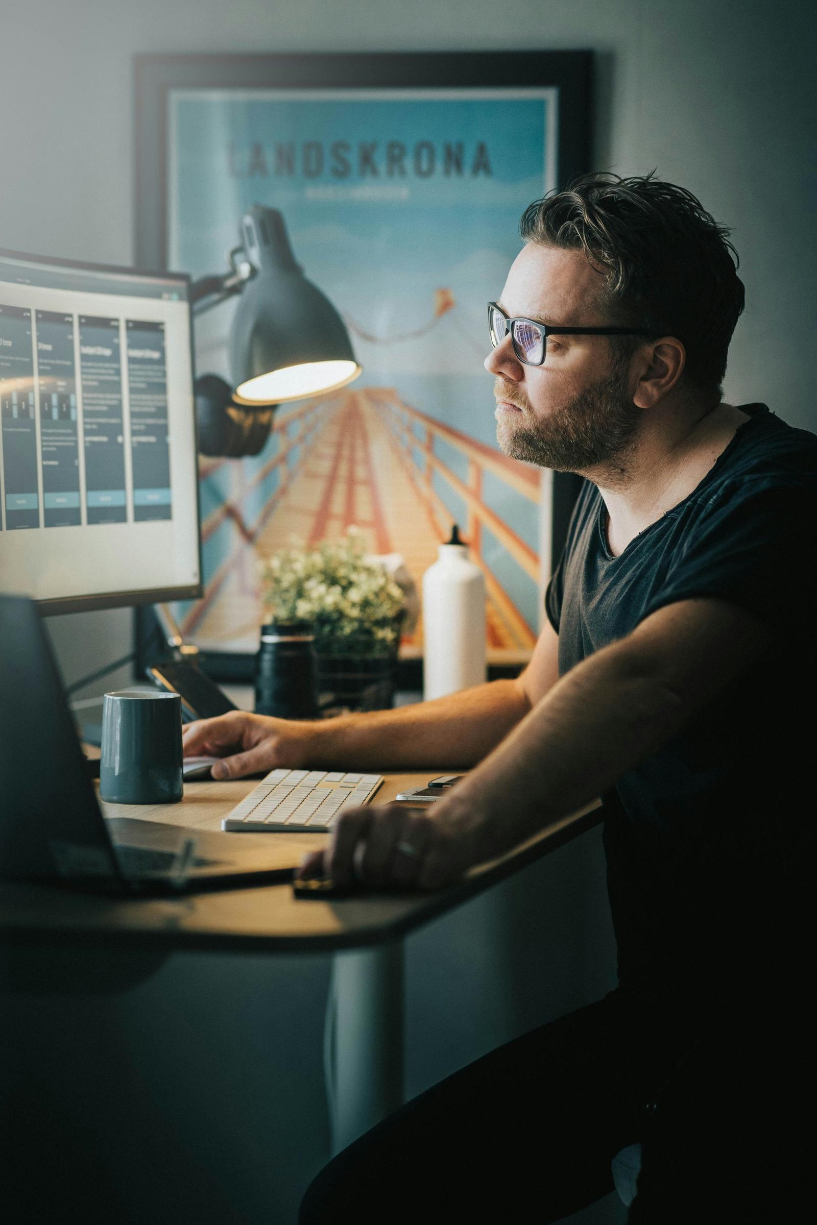 Man working at a desk with analytics dashboards on two monitors, framed poster behind him