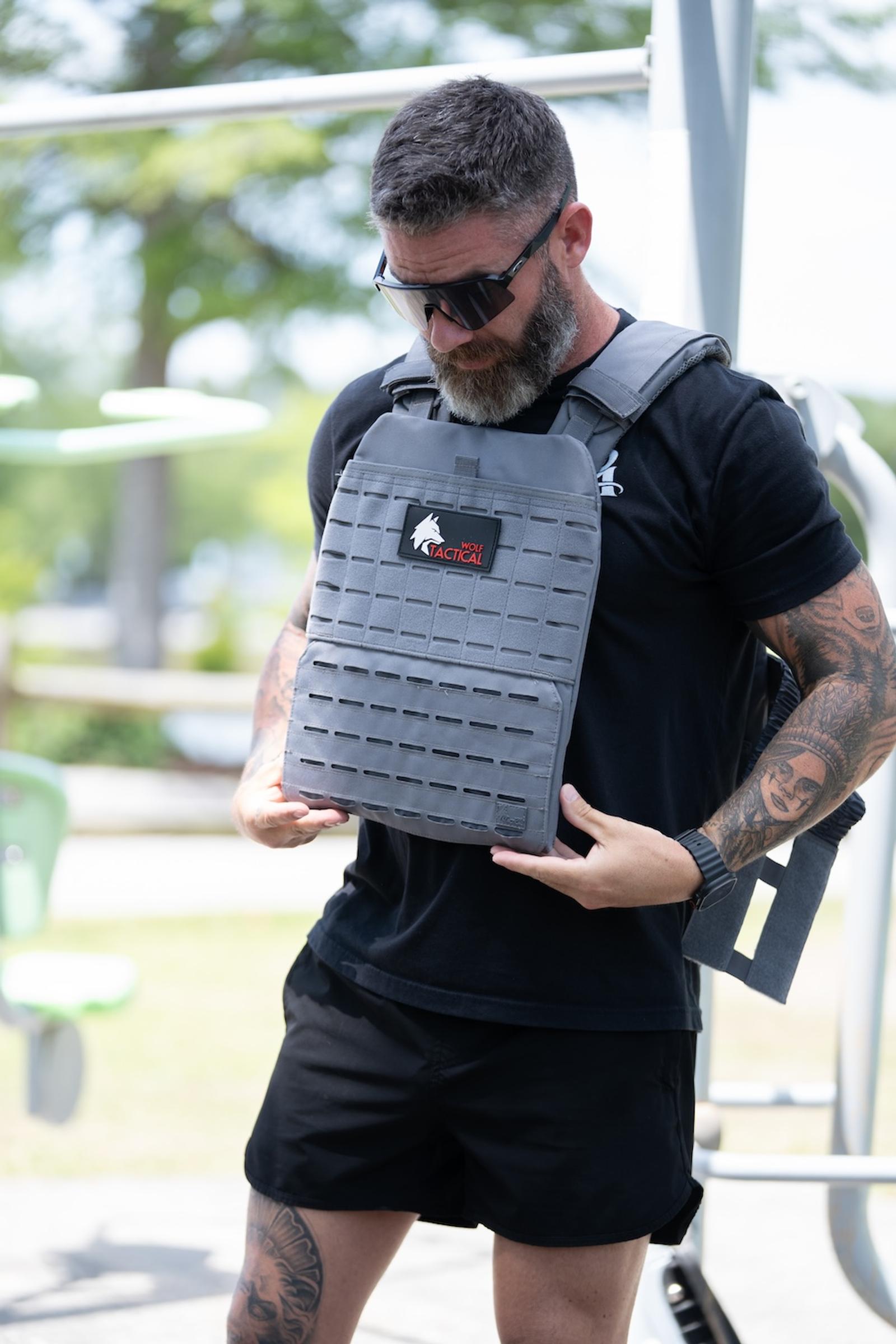 Man holding a gray Wolf Tactical weighted plate carrier vest at an outdoor gym