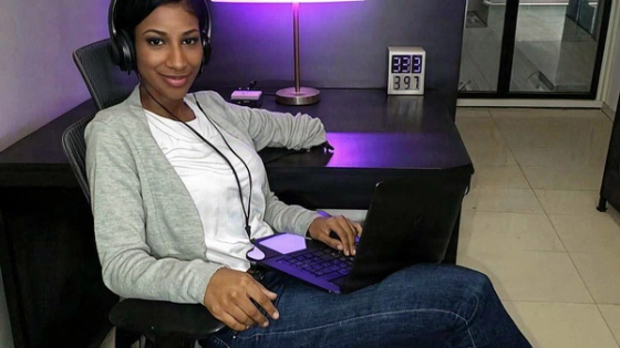 Woman with headphones and a laptop at a desk lit by purple neon