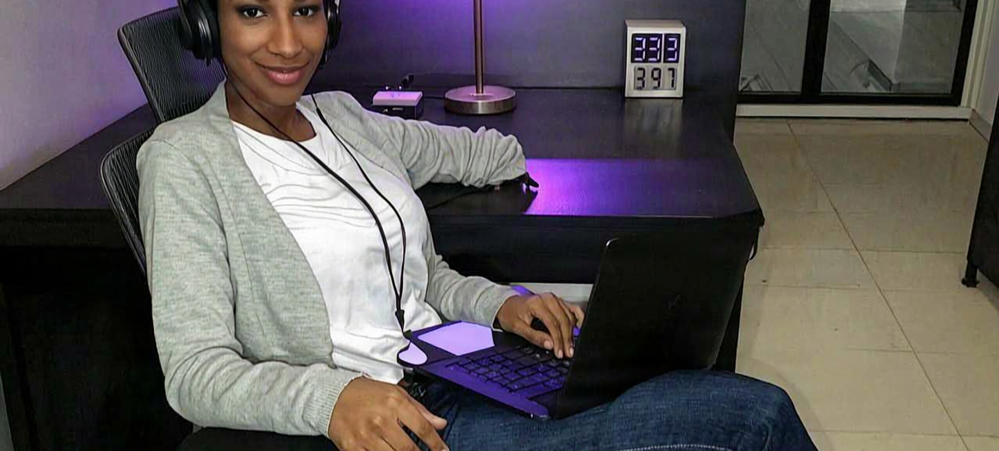 Woman with headphones and a laptop at a desk lit by purple neon