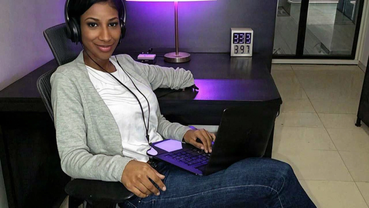 Woman with headphones and a laptop at a desk lit by purple neon
