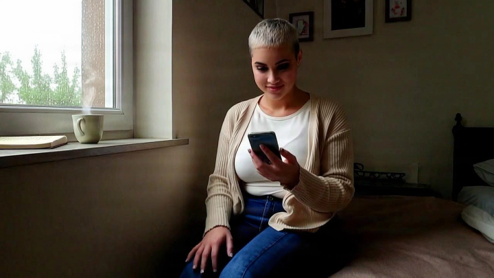 Woman smiling at her phone by a rainy window
