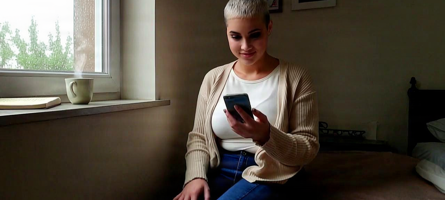 Woman smiling at her phone by a rainy window