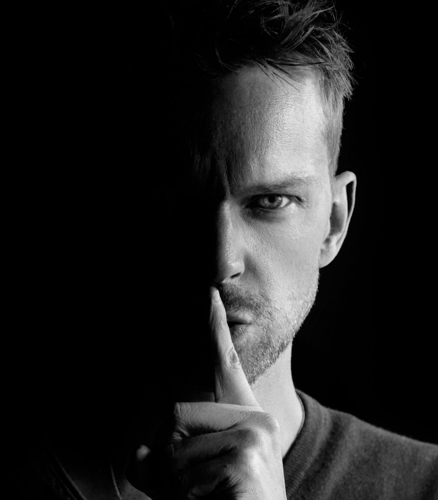 A man with a dark background shhh-ing people