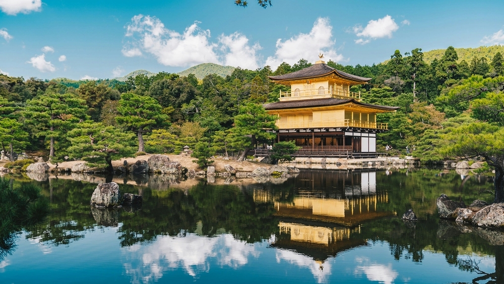 Golden Kinkaku-ji temple reflected in a pond amidst lush green trees.