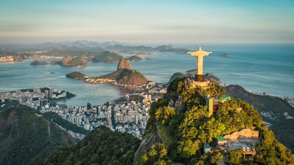 Aerial view of Christ the Redeemer statue overlooking Rio de Janeiro, with Sugarloaf Mountain and Guanabara Bay.