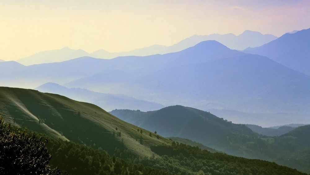 Layered mountain landscape with green hills and increasingly hazy blue peaks fading into the distance.
