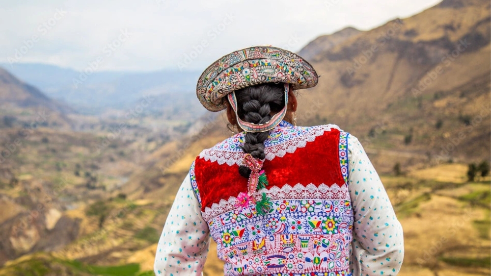An Indigenous woman and child in traditional dress sorting broad beans on the ground by a lake.
