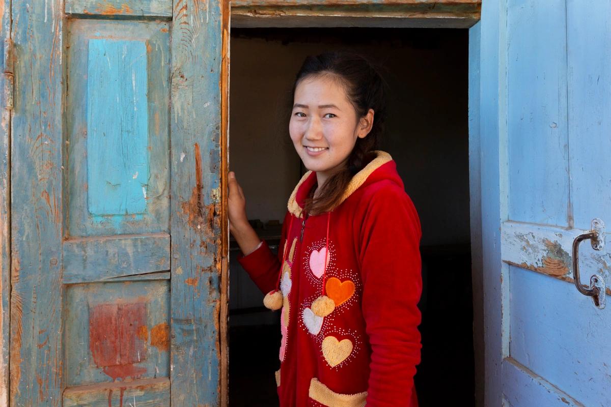 A smiling young woman in a red heart-decorated hoodie stands in an old blue doorway.