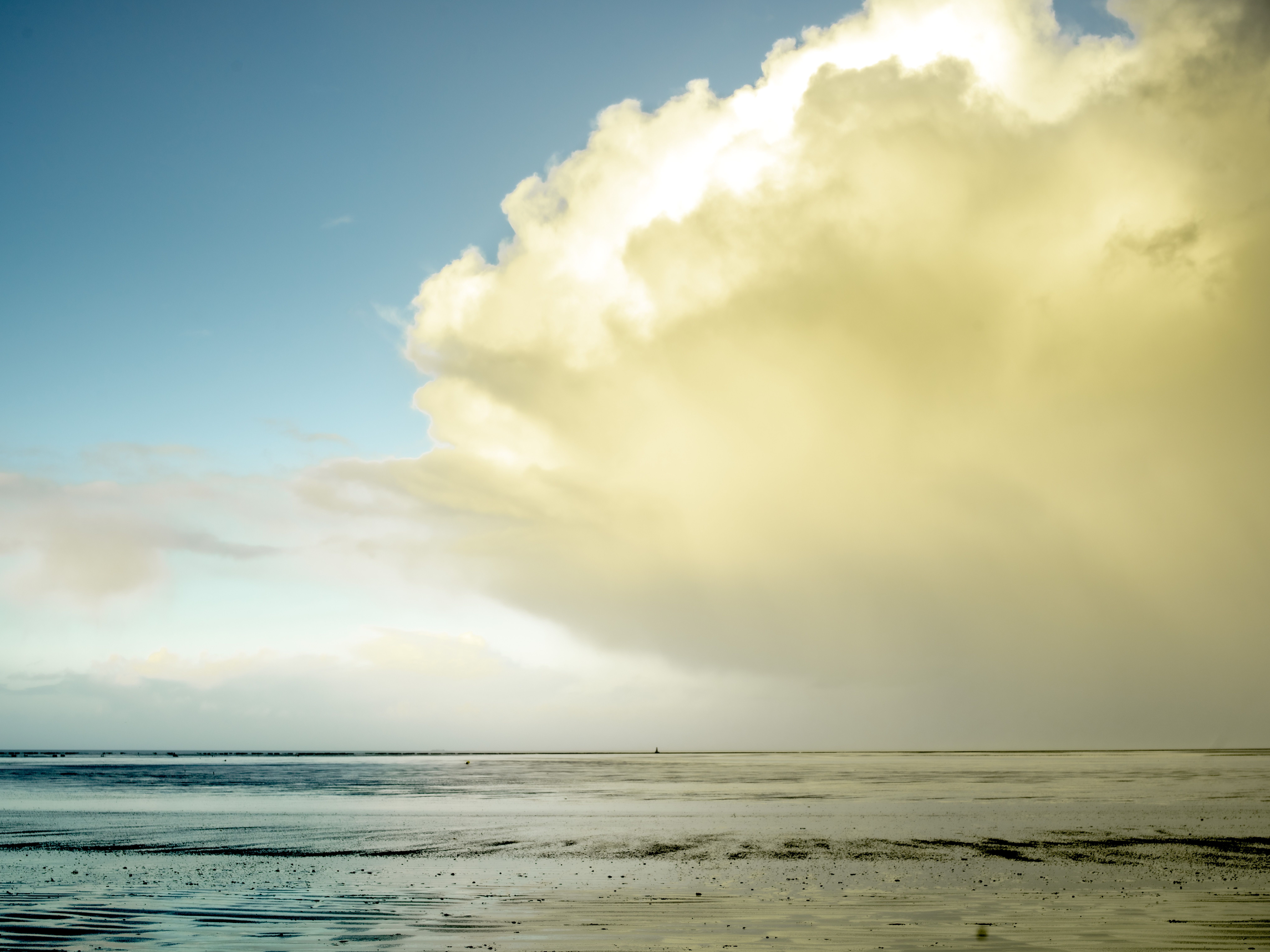 Small boats moored to wooden poles in a turquoise bay with a sandy beach and rocky cliffs.