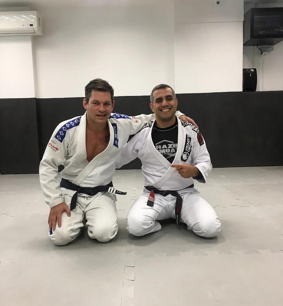Two men in martial arts gis grappling on the floor, one applying a leg-based hold to the other.