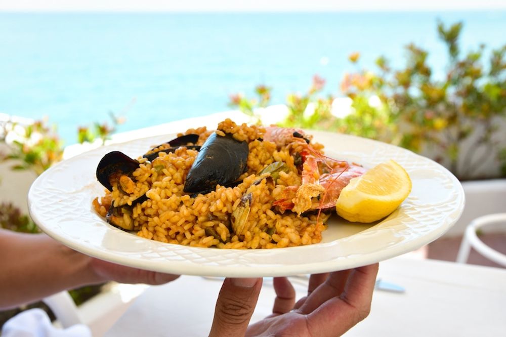 Paella &auml;ts med f&ouml;rdel varm i skuggan p&aring; en strandrestaurang, eller varf&ouml;r inte kall p&aring; en medhavd picknick bredvid havet?