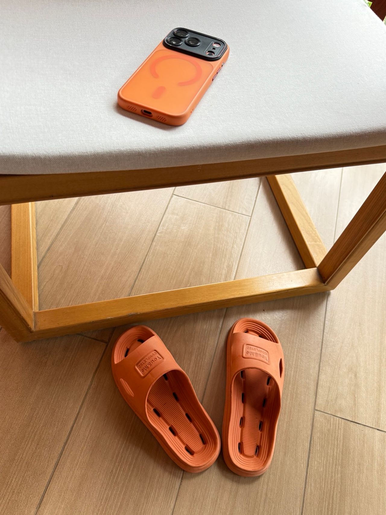 iPhone dans une coque orange posé à côté d’une paire de tongs orange, utilisées comme clin d’œil visuel à l’écosystème d’accessoires Apple.
