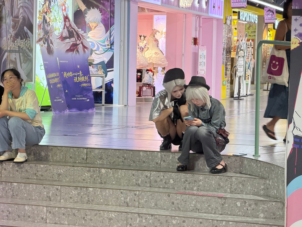 Deux jeunes personnes en tenue stylisée assises dans un espace commercial consacré à la pop culture à Changsha.