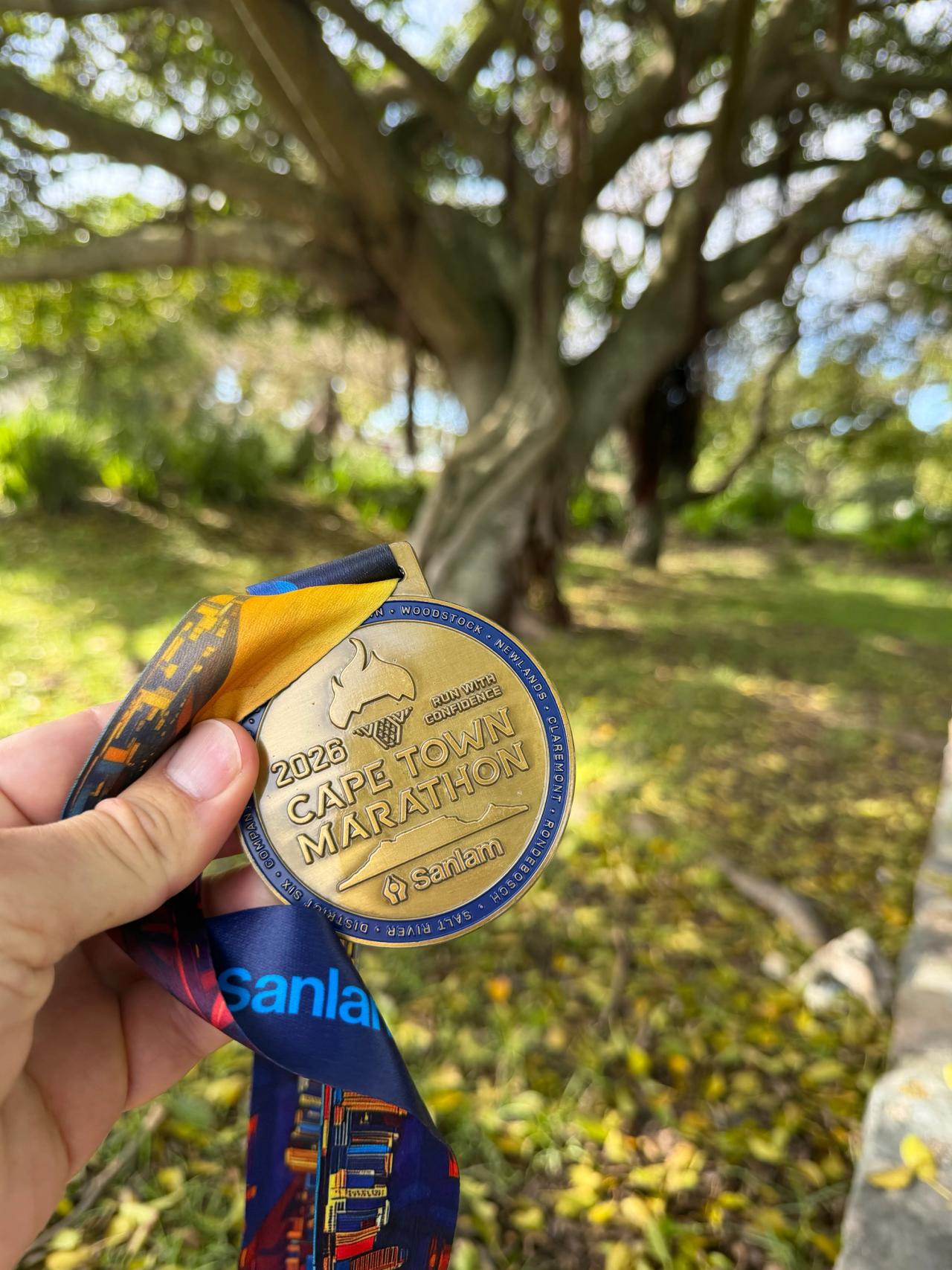 Médaille du Sanlam Cape Town Marathon 2026 tenue devant un arbre au Cap.