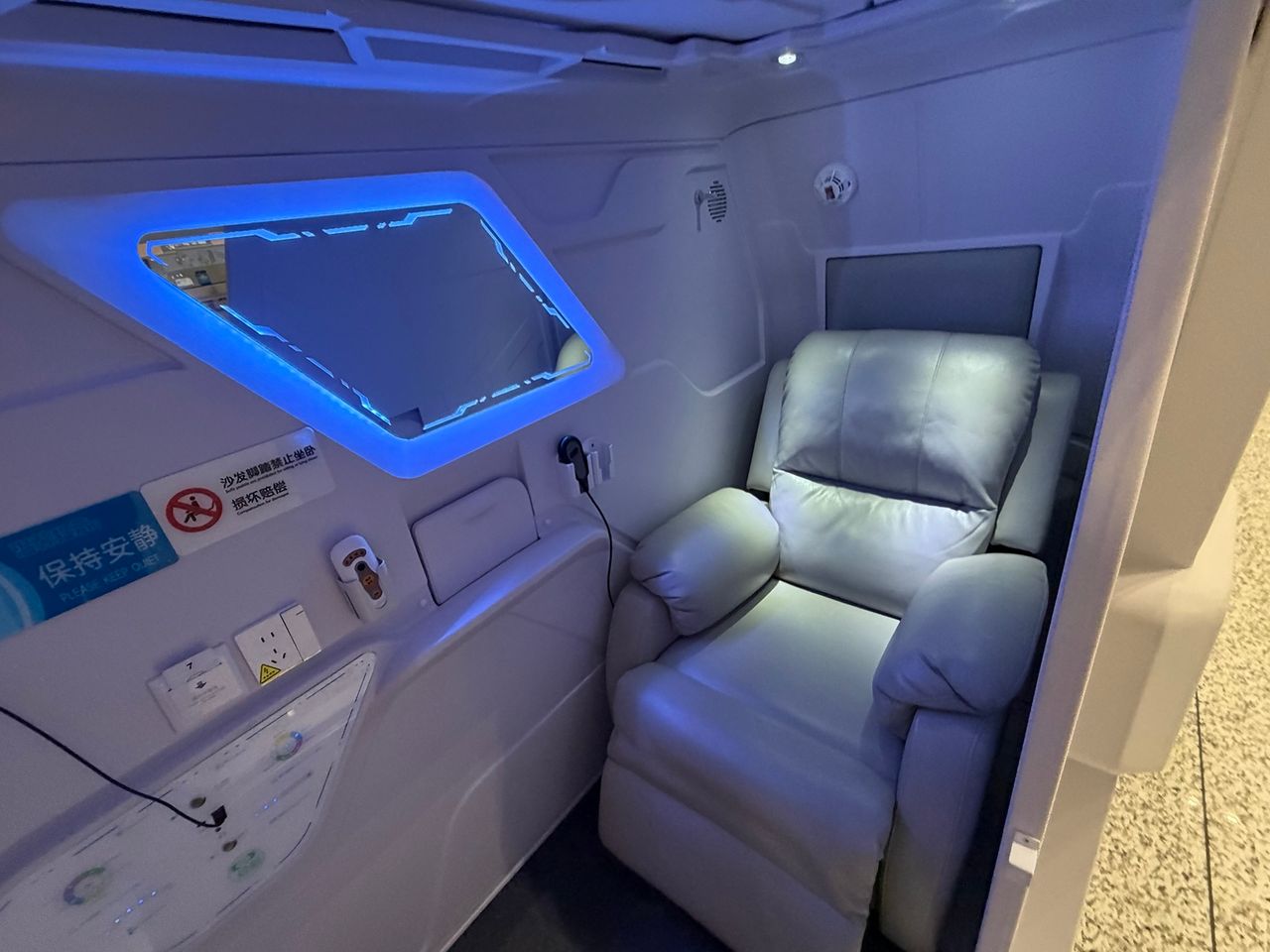 Intérieur d’une cabine de repos avec fauteuil inclinable, écran et équipements électriques.