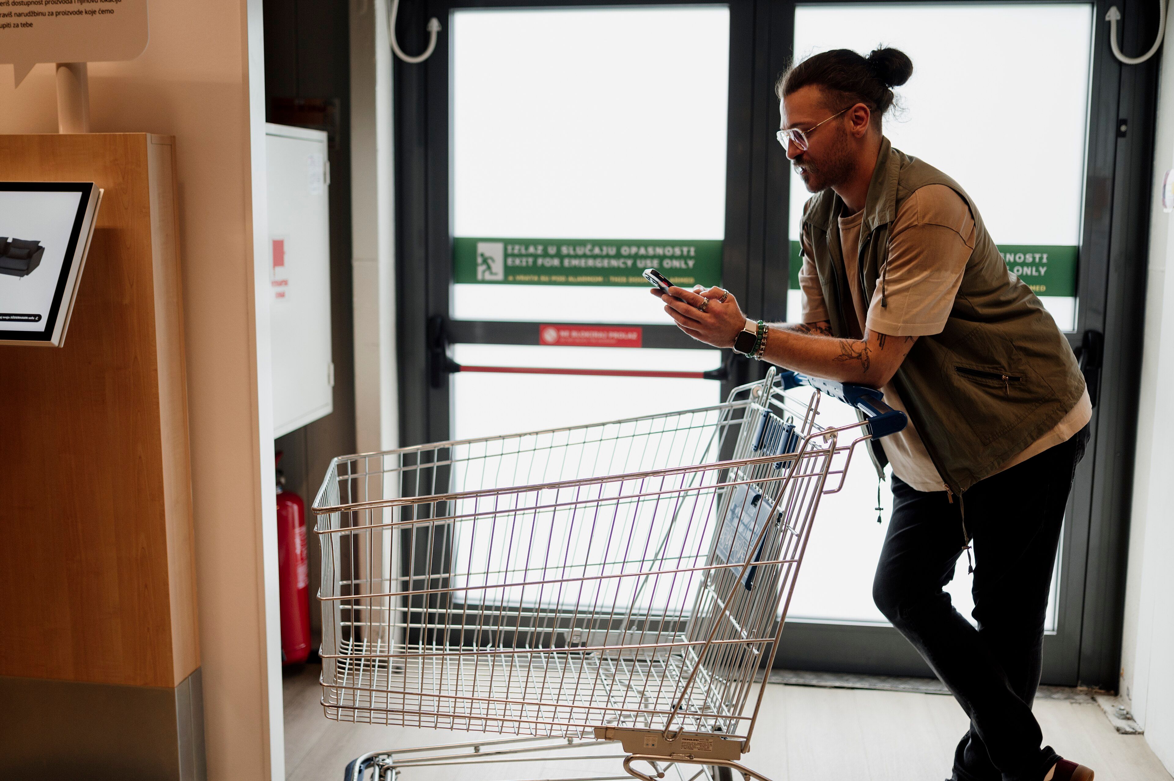 Client consultant son smartphone tout en poussant un chariot dans un supermarché.