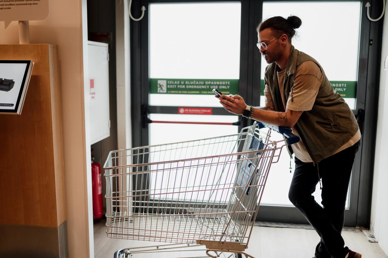 Client consultant son smartphone tout en poussant un chariot dans un supermarché.