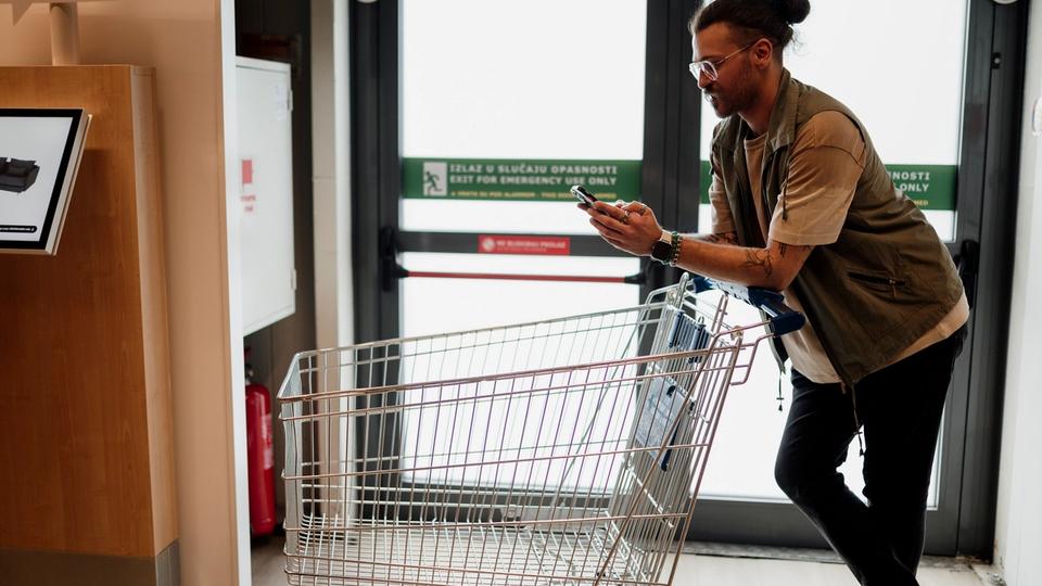 Client consultant son smartphone tout en poussant un chariot dans un supermarché.