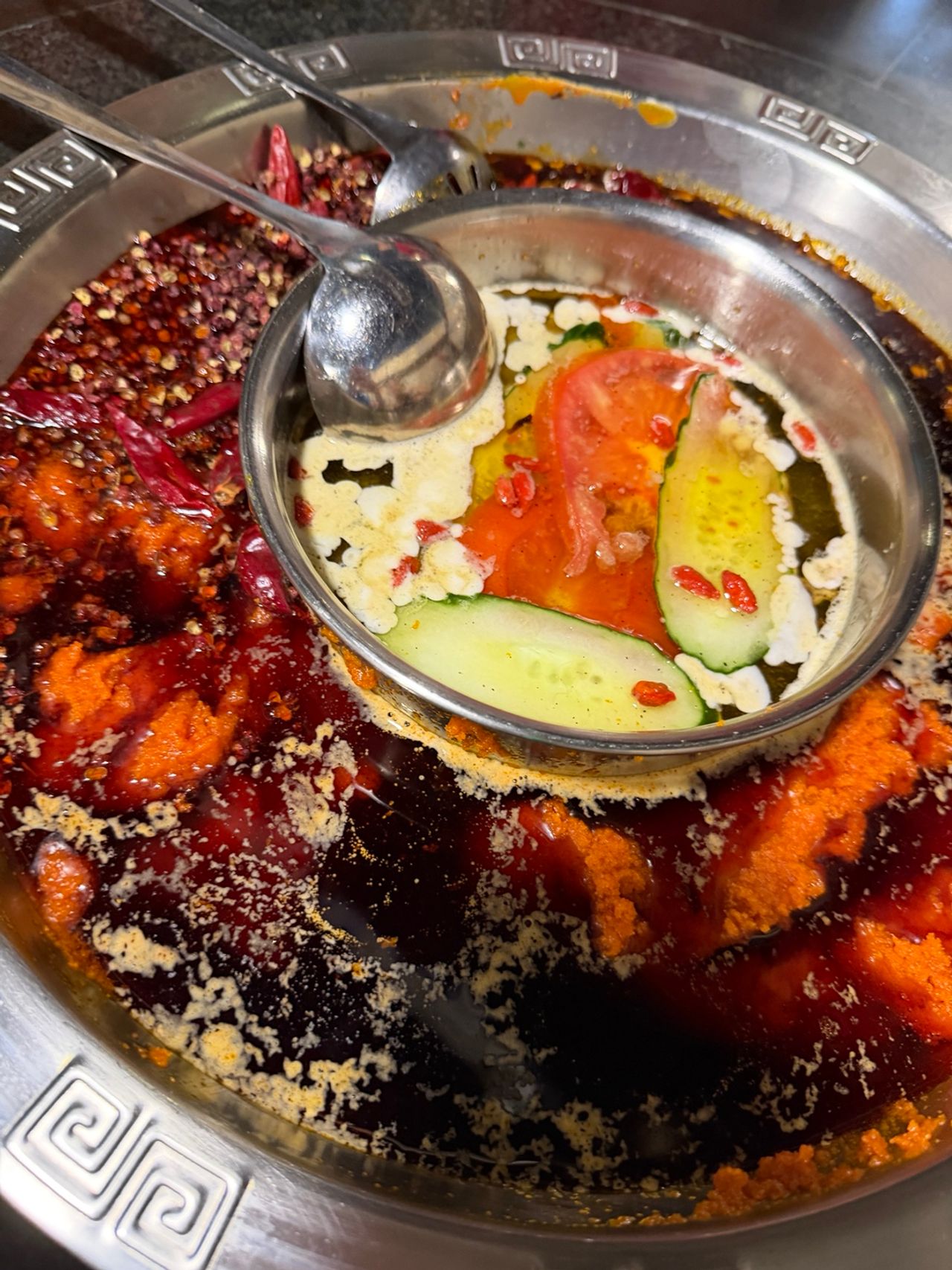Gros plan d’un hot pot de Chongqing avec bouillon rouge très épicé, piments et poivre du Sichuan autour d’un compartiment clair central.