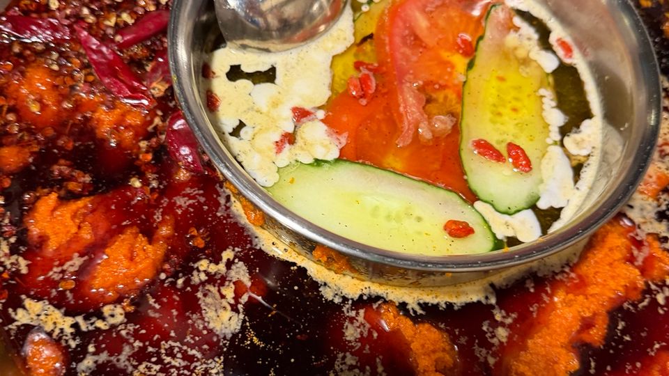 Gros plan d’un hot pot de Chongqing avec bouillon rouge très épicé, piments et poivre du Sichuan autour d’un compartiment clair central.