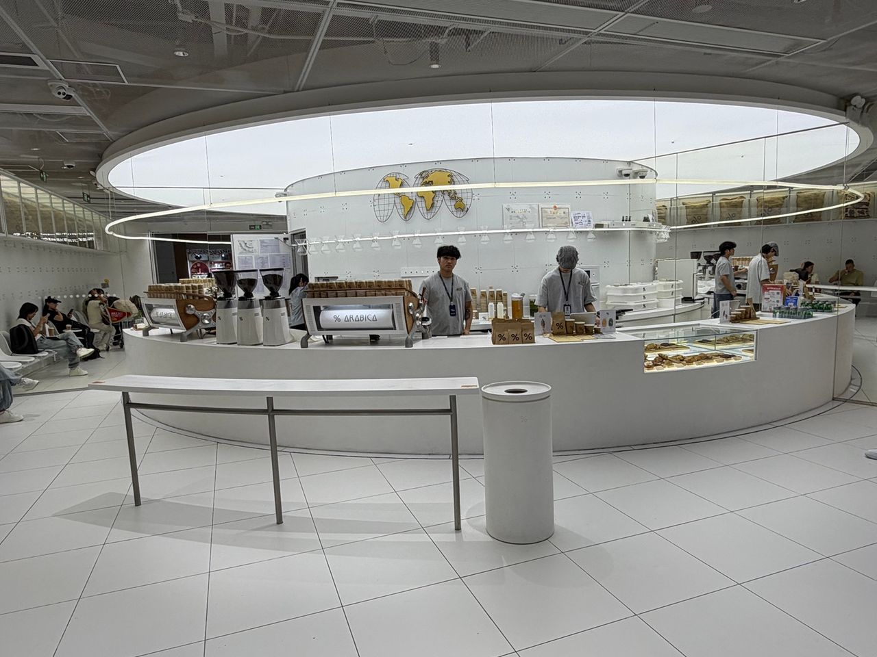Vue large de l’espace % Arabica de Guangzhou Baiyun, avec comptoir courbe, miroirs et grand anneau lumineux.