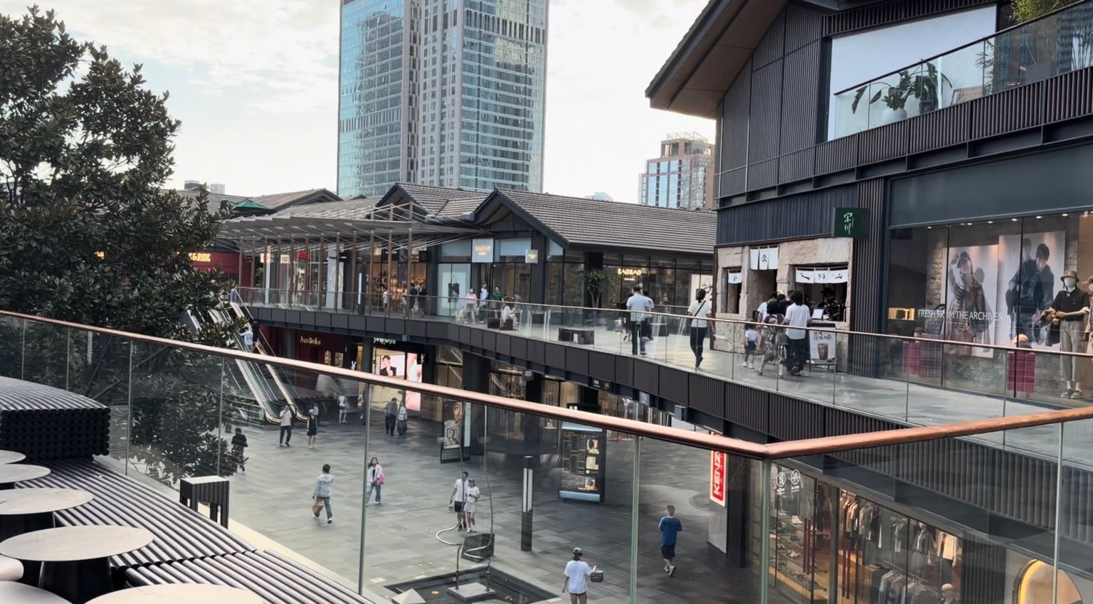 Vue terrain de Taikoo Li Chengdu avec bâtiments commerciaux bas, cheminements ouverts et tours de grande hauteur en arrière-plan.