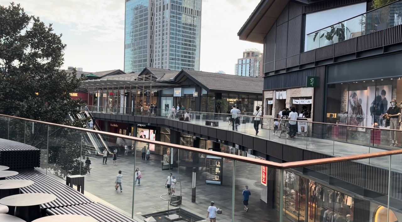 Vue terrain de Taikoo Li Chengdu avec bâtiments commerciaux bas, cheminements ouverts et tours de grande hauteur en arrière-plan.