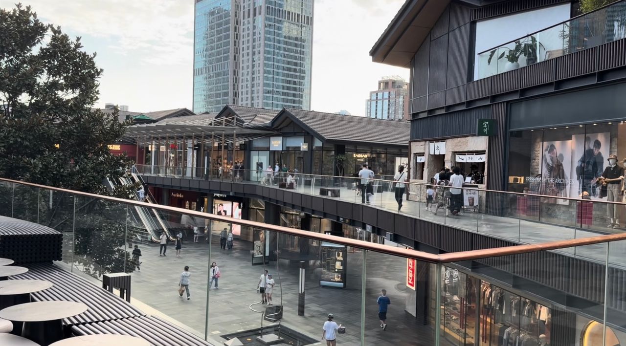 Vue terrain de Taikoo Li Chengdu avec bâtiments commerciaux bas, cheminements ouverts et tours de grande hauteur en arrière-plan.