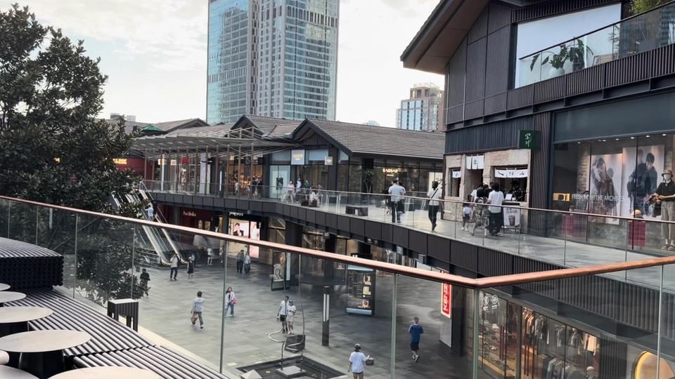 Vue terrain de Taikoo Li Chengdu avec bâtiments commerciaux bas, cheminements ouverts et tours de grande hauteur en arrière-plan.