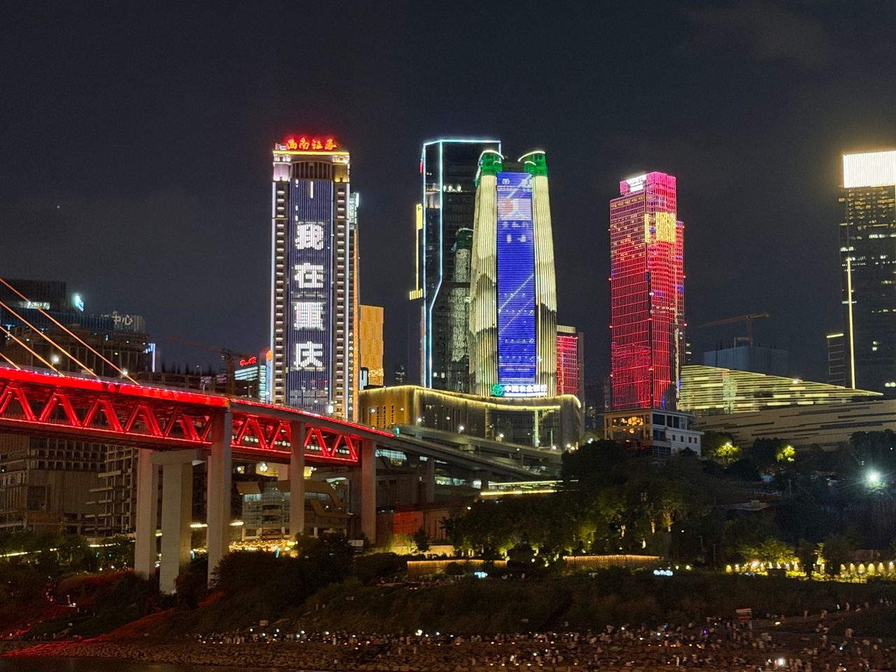 Vue nocturne de Chongqing avec une infrastructure rouge au premier plan et des gratte-ciel illuminés à l’arrière-plan.