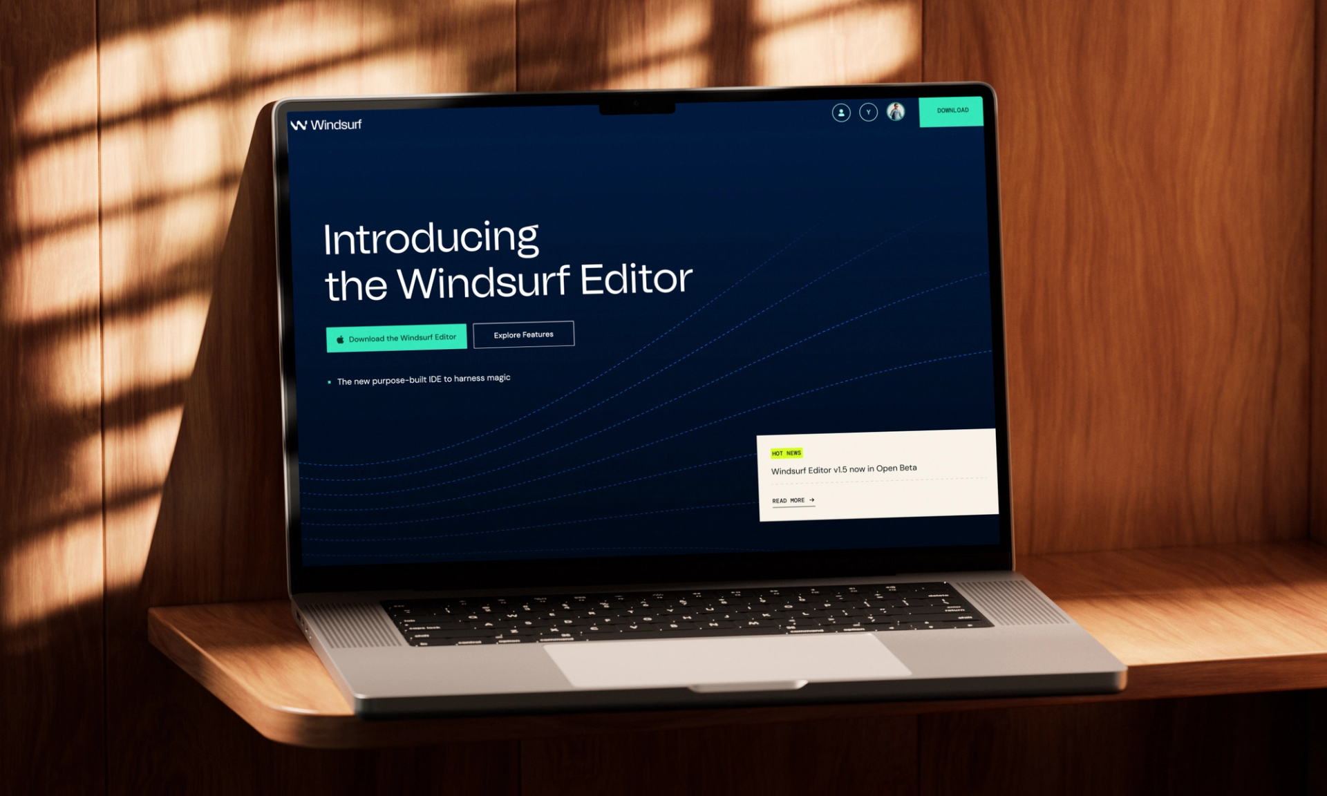 A laptop sits on a wooden desk, displaying a scroll through the Windsurf Editor landing page. The initial screen reads “Introducing the Windsurf Editor” with buttons to download the app or explore features. 