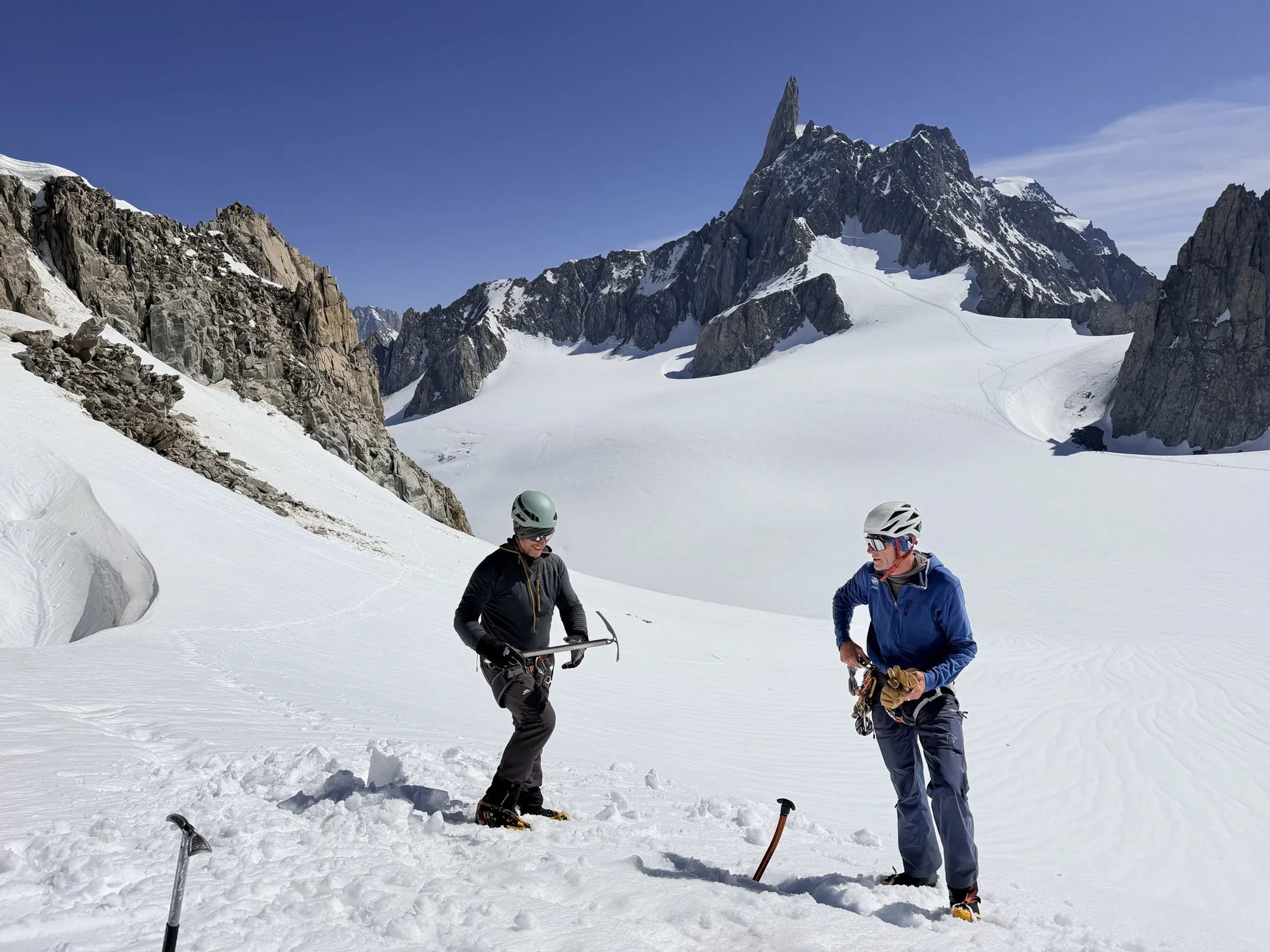 Two people equipped with ice axes and climbing gear on a snowy alpine glacier