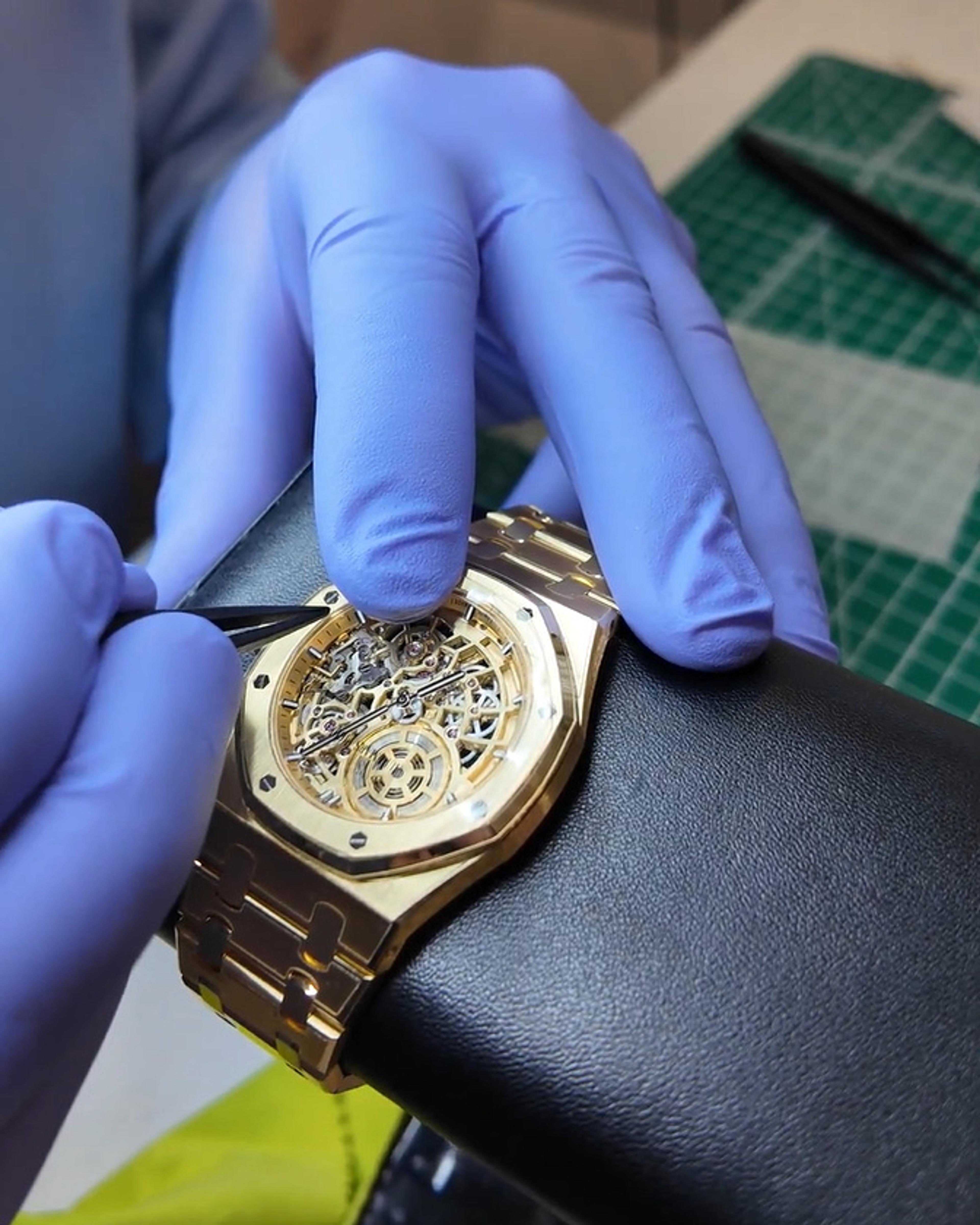 Gloved hands fitting film to a gold skeleton watch on a leather cushion