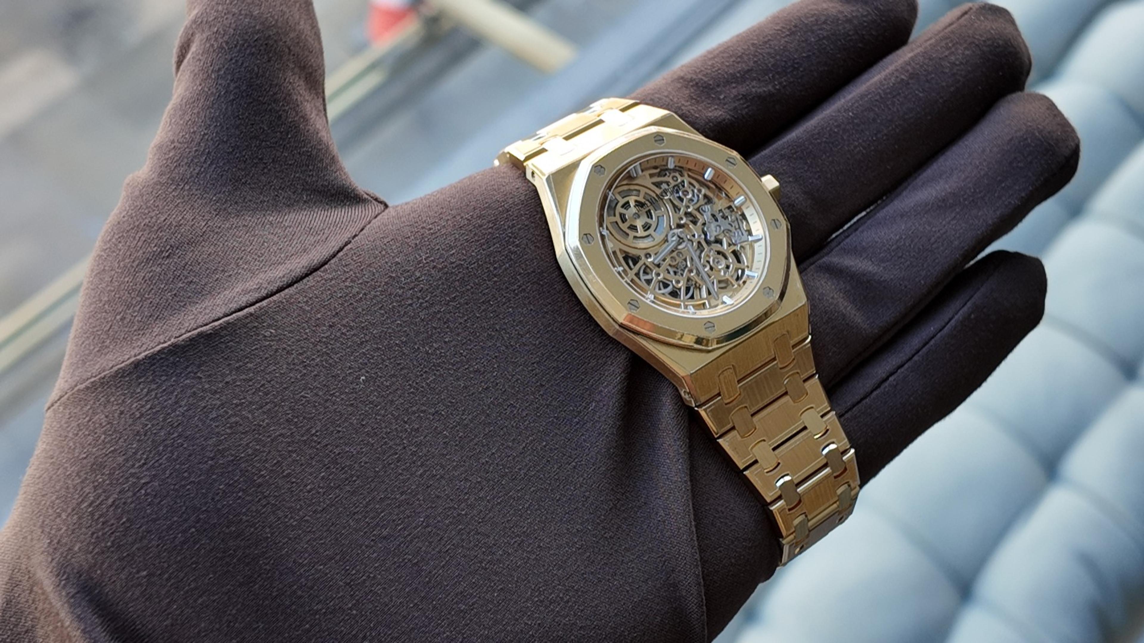 A gold skeleton watch resting on a dark gloved hand