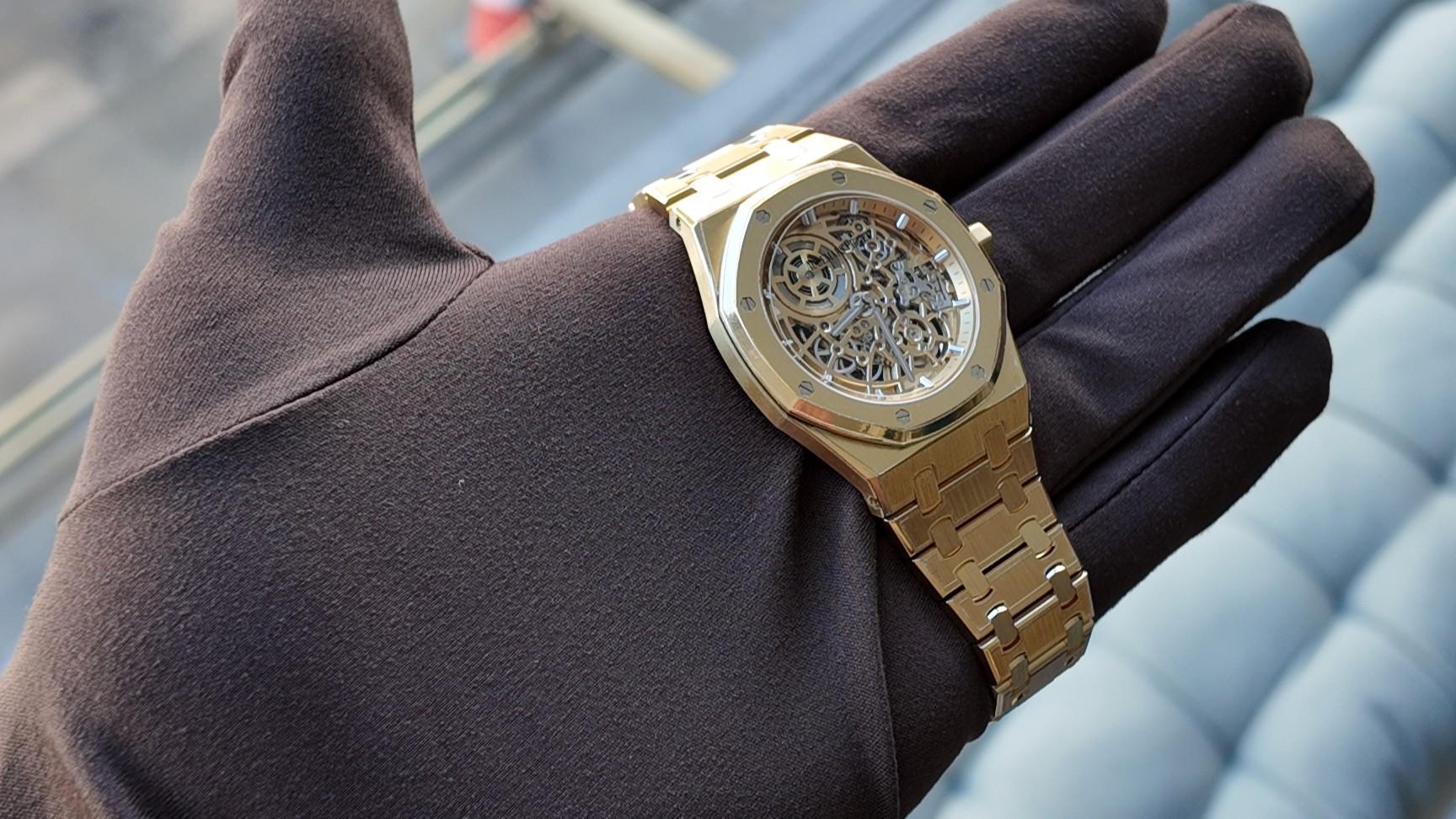 A gold skeleton watch resting on a dark gloved hand
