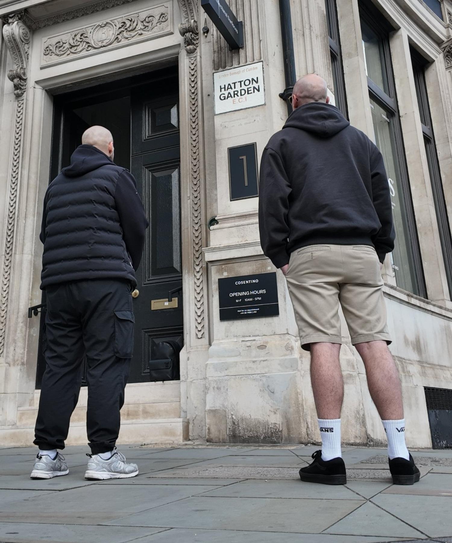 Jason and James, seen from behind, outside a stone building on a London street corner
