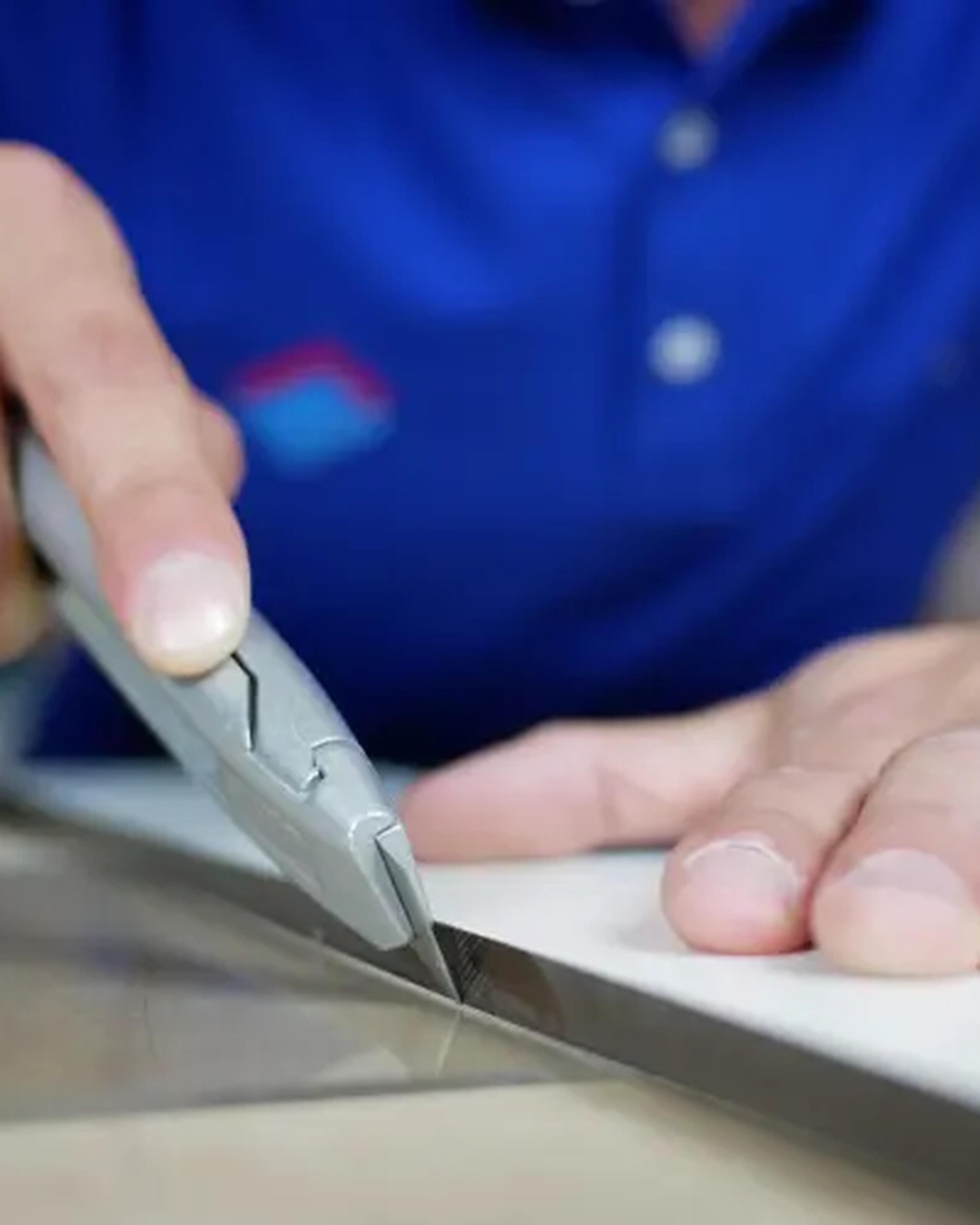 A hand cutting a sheet of film to size with a craft knife