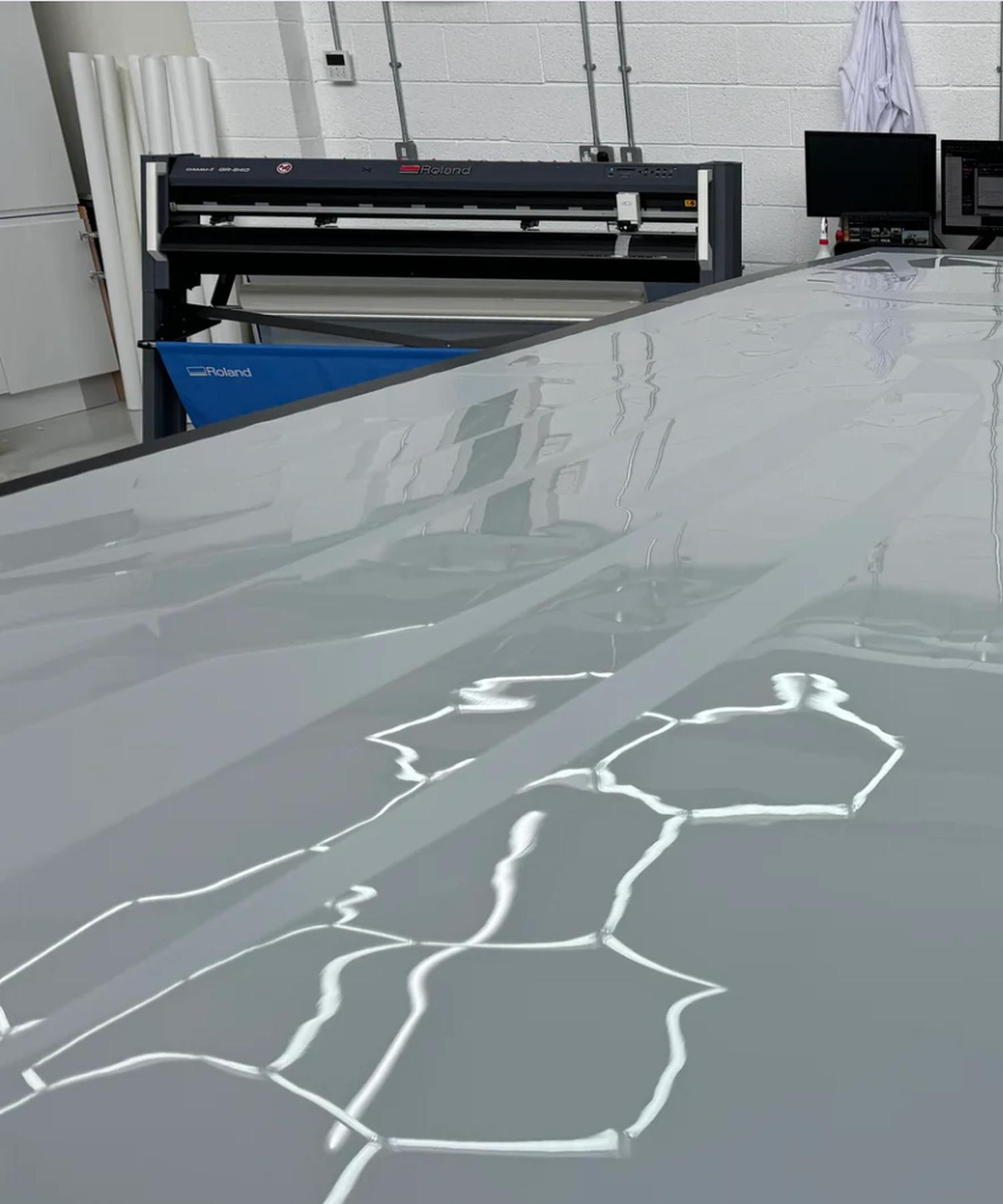 A sheet of clear film on a large cutting table, with a plotter cutter behind