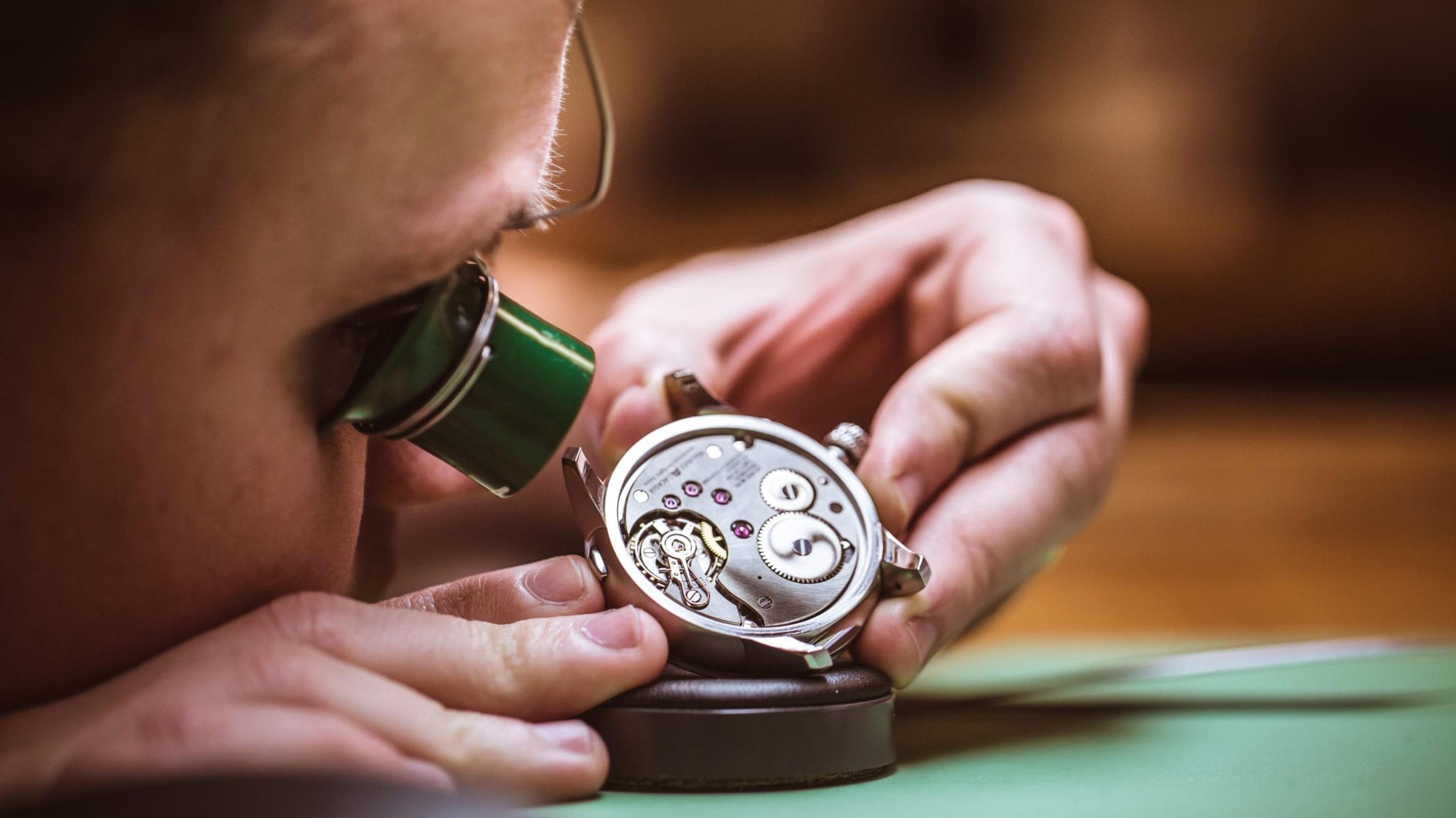 A watchmaker examining a watch movement through a loupe